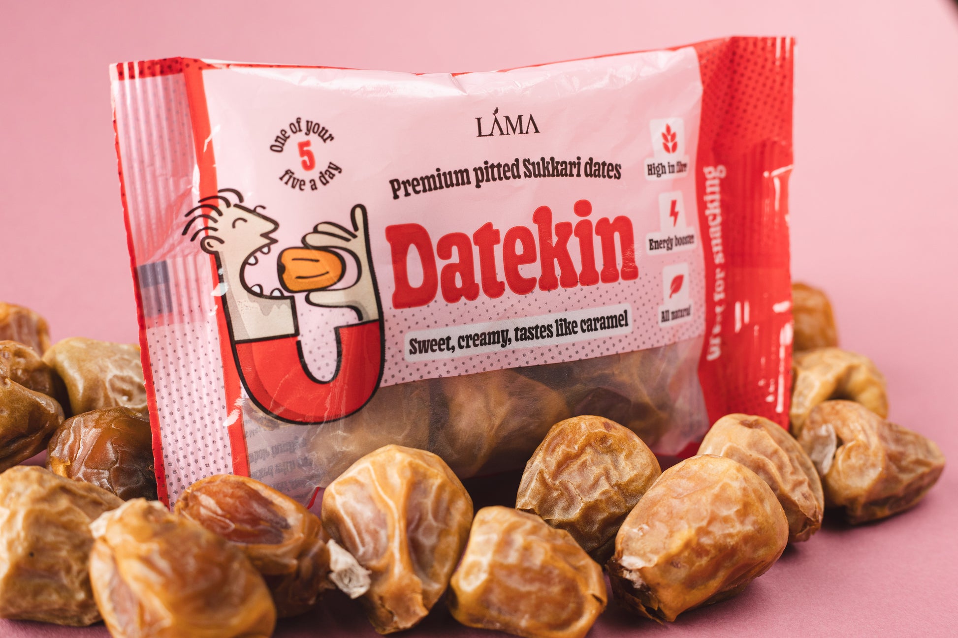 Datekin Premium Pitted Sukkari Dates are nestled among spilled dates. This nutritious snack is in striking red and white packaging with a fun cartoon character, emphasizing sweet, creamy, tastes like caramel and its one of your 5 a day. Ideal for easy shelf display and quick pick-ups.