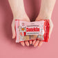 Hands hold a red packet of Datekin Premium Pitted Sukkari Dates against a pink background, showcasing the natural sweetness of healthy dates with illustrations and text including sweet, creamy, gooey, rich caramel.